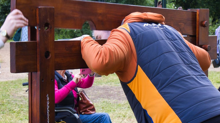 Photo of man with head and arms inserted into wooden stocks